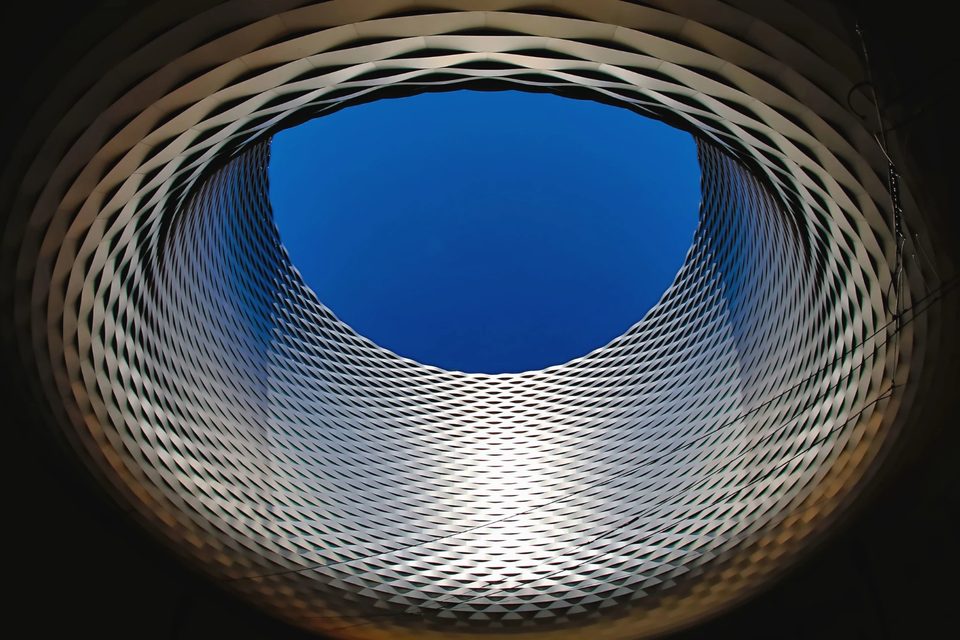 Cubierta circular de una estructura metálica vista desde abajo, abierta a un óculo de cielo azul